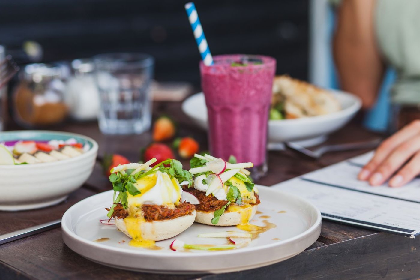 An overhead view of a brunch spread with eggs, fresh fruit, and coffee on a caf&eacute; table