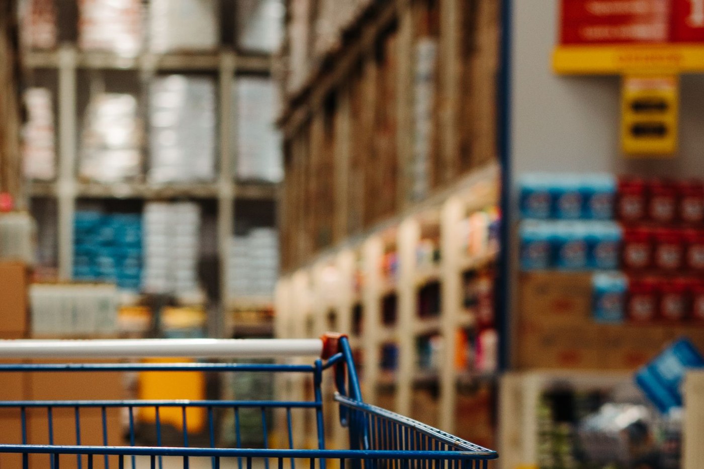 A shopping cart in the foreground of a warehouse-style retail store aisle lined with tall bulk product shelving, used here as a representative image of the kind of warehouse club Lawrenceville has approved