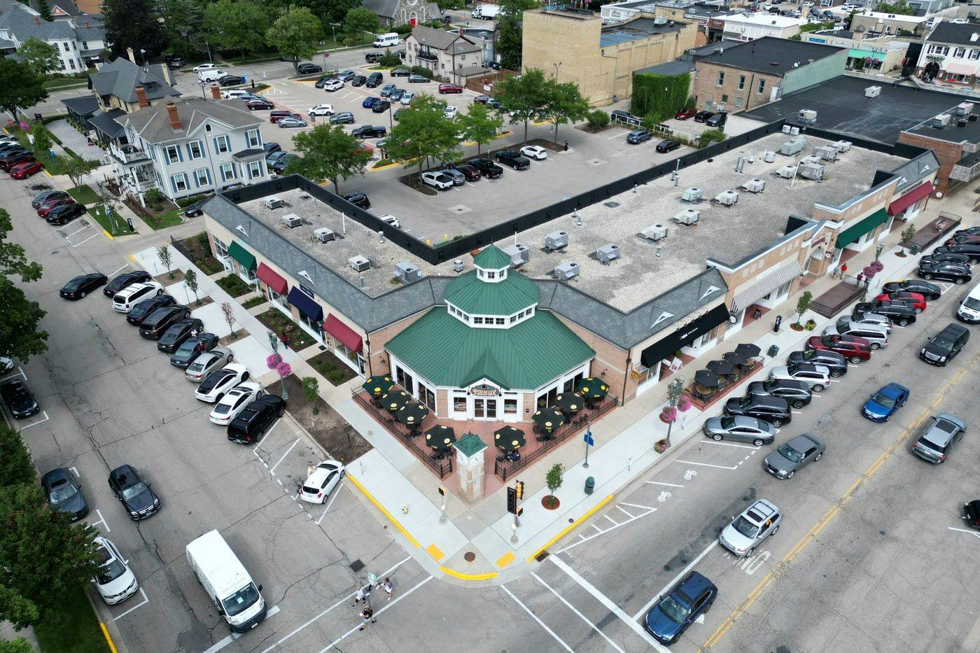Aerial view of a tree-lined suburban shopping center with cars in the parking lot