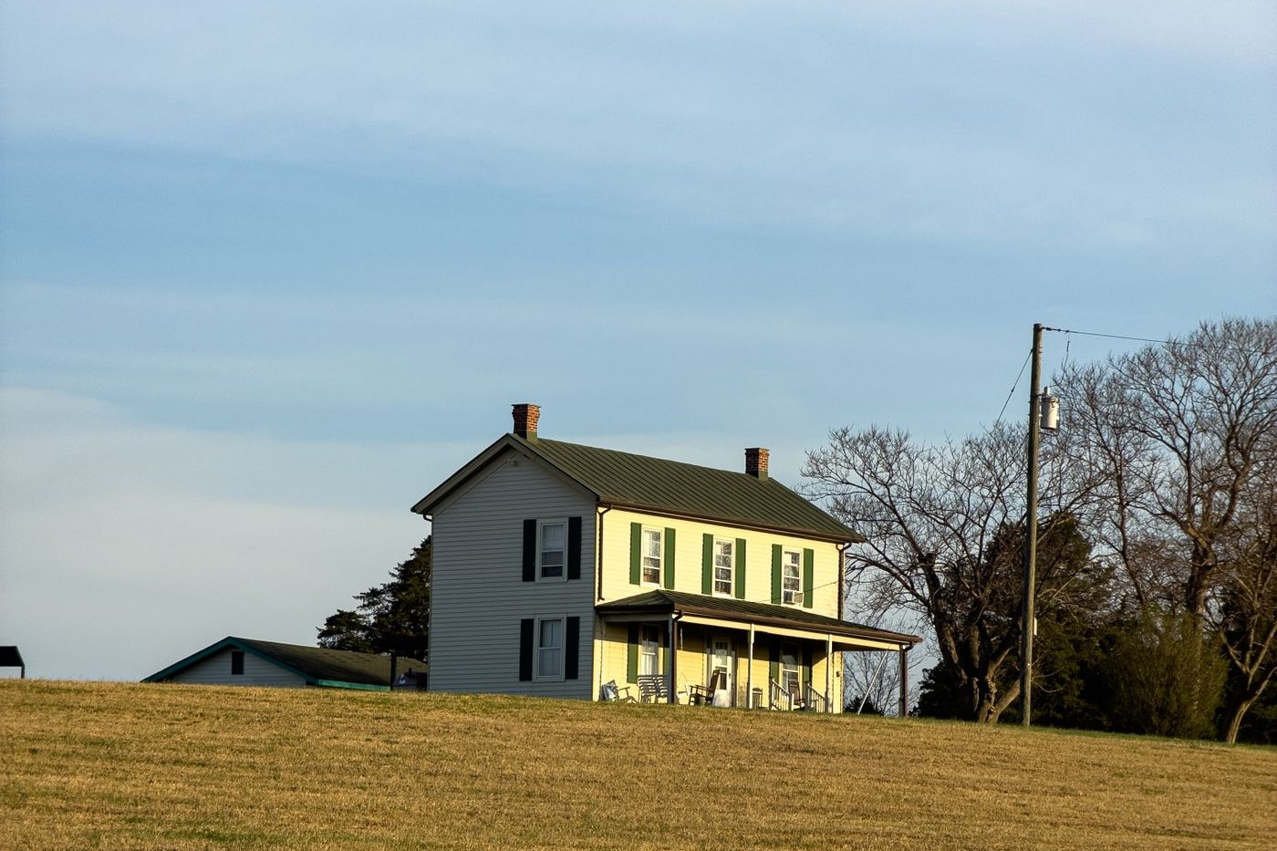 A two-story white farmhouse standing alone in an open grassy field, used here as a representative image